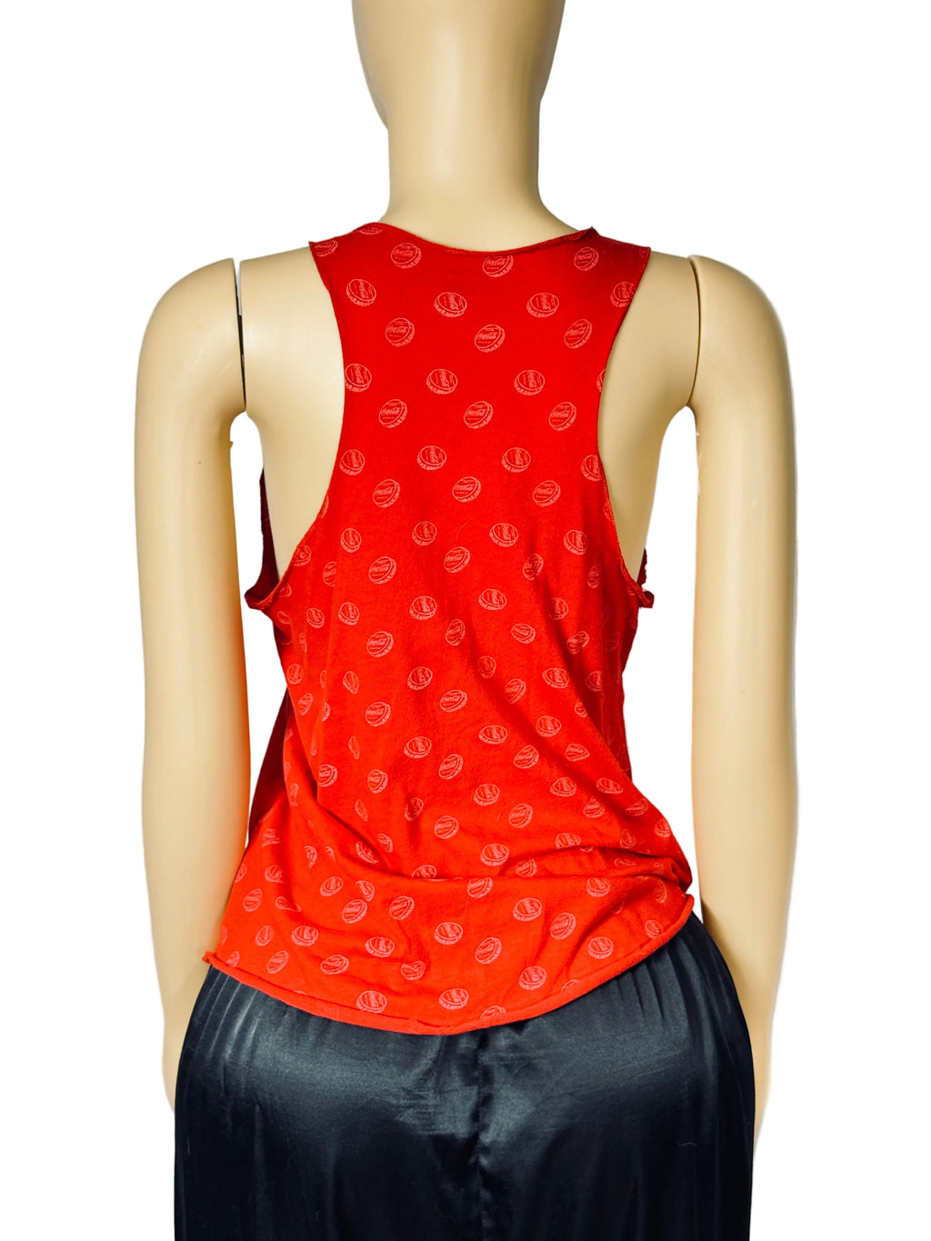 A red sleeveless tank top with a repeating tonal circular pattern, displayed on a beige mannequin from the back. The top is paired with dark blue pants against a light gray fabric backdrop.