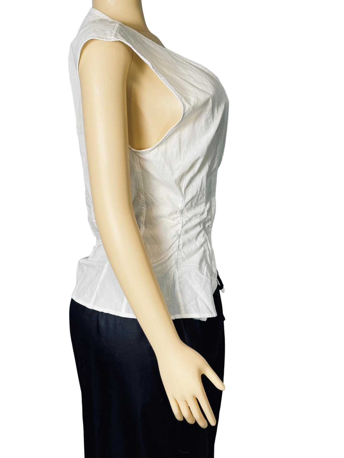 A white sleeveless top with a dramatic plunging neckline, displayed on a beige mannequin torso against a light gray fabric backdrop.