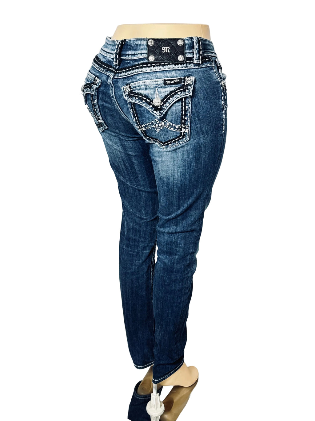 Blue denim jeans with decorative silver rhinestone stitching on the back pockets, displayed on a mannequin from a rear three-quarter view against a white fabric backdrop.