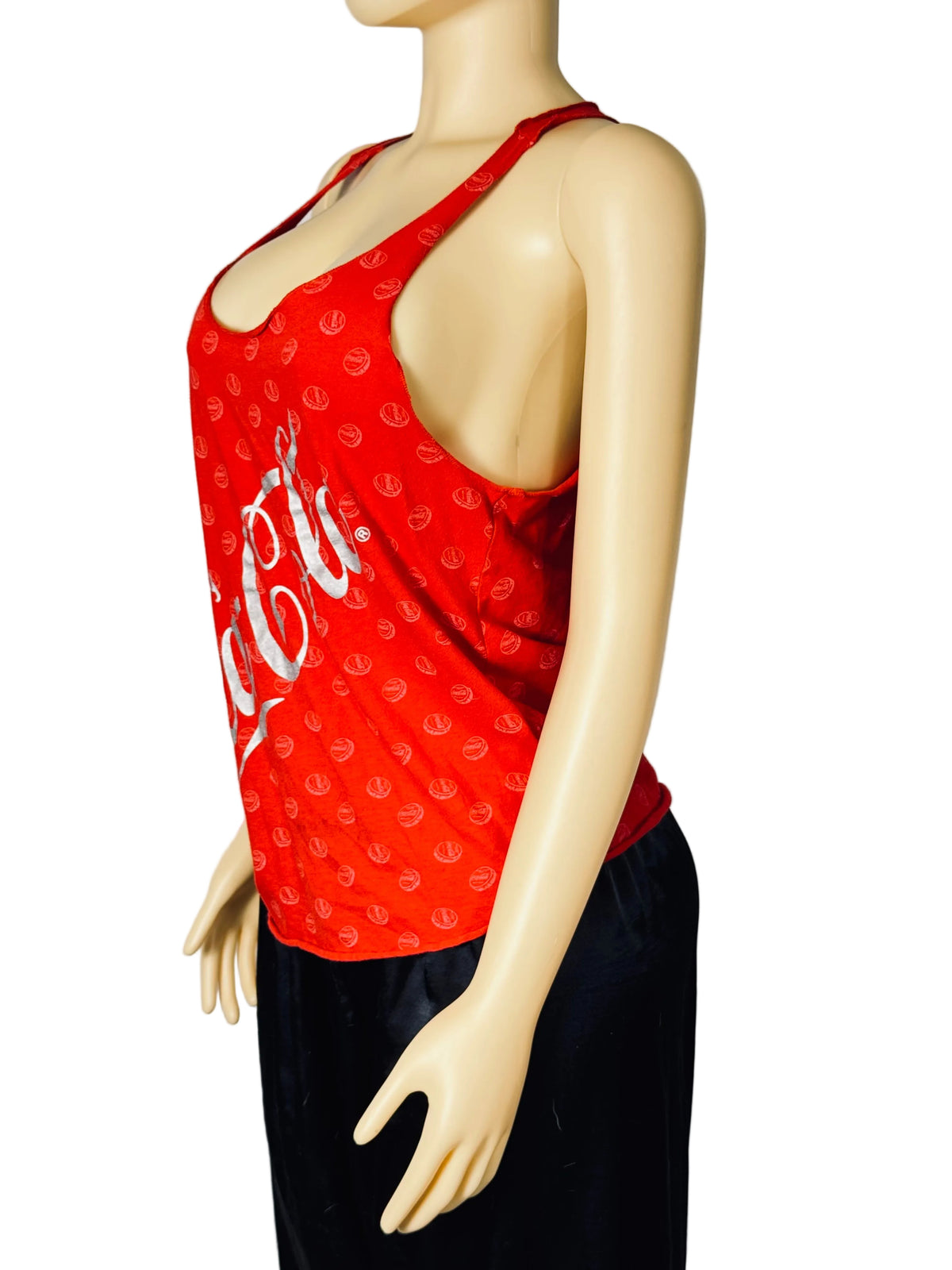 A red sleeveless halter-style top with a white Coca-Cola script and small repeating logo pattern, displayed on a beige mannequin torso against a light gray fabric backdrop.
