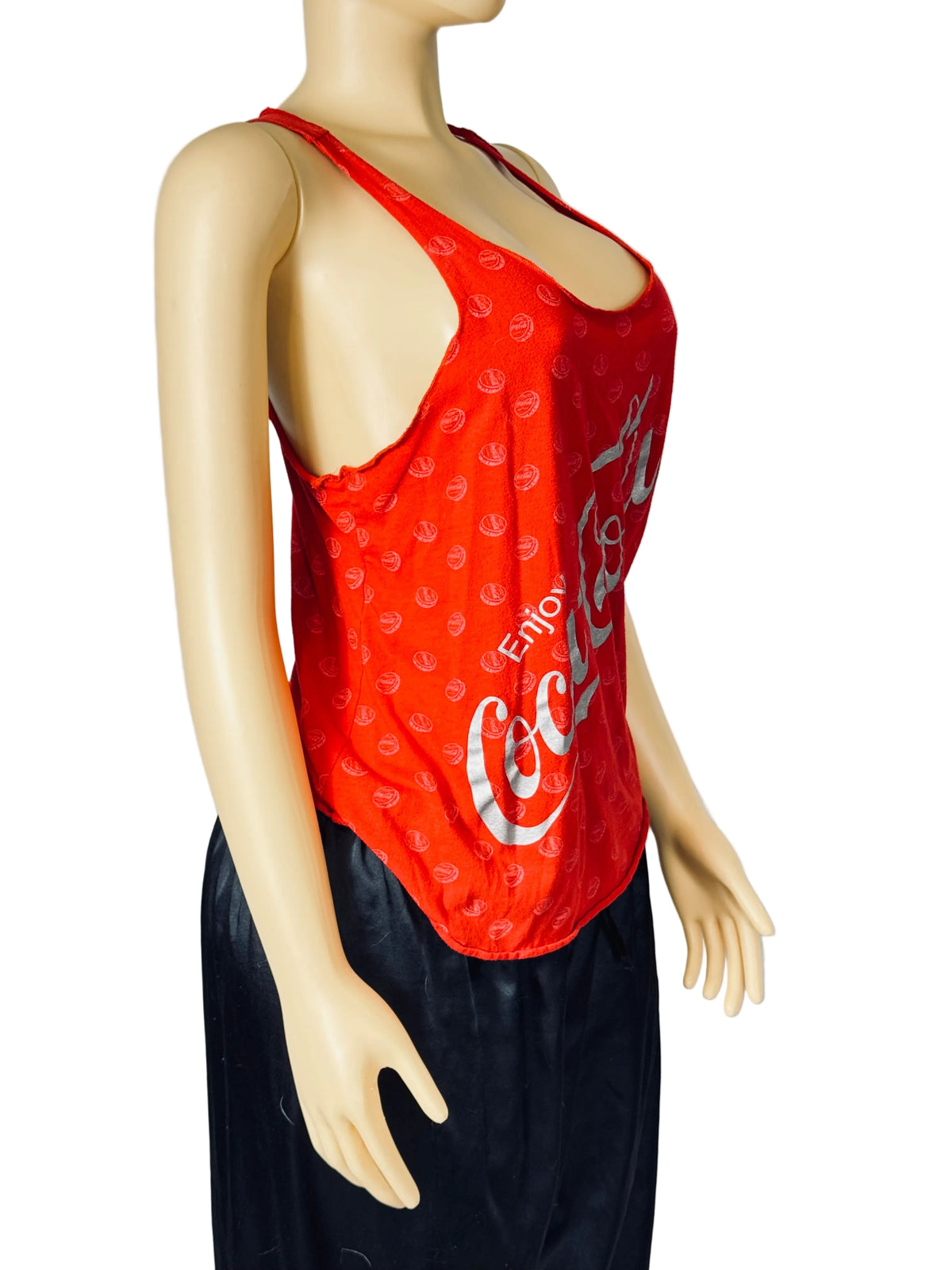 A red sleeveless tank top with a Coca-Cola logo and pattern, displayed on a beige mannequin torso against a light gray background.