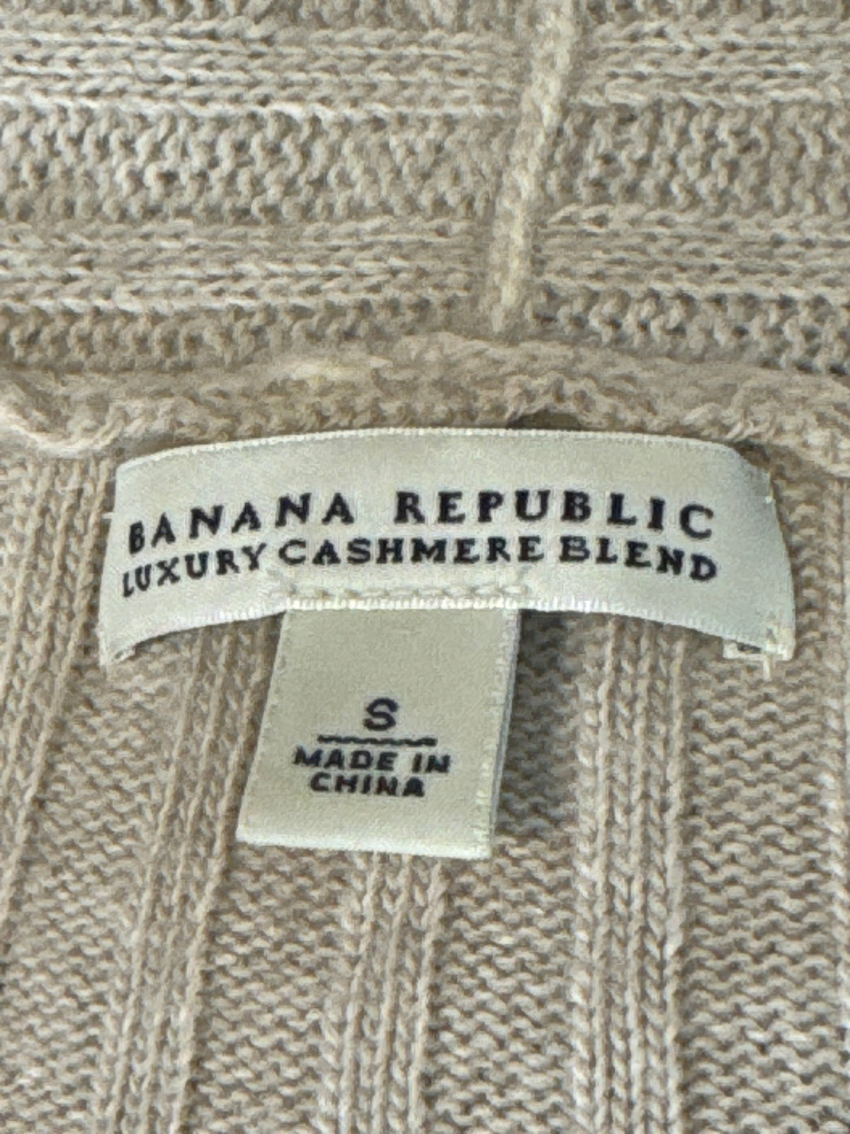 Close-up of a beige knit sweater label reading BANANA REPUBLIC LUXURY CASHMERE BLEND, with a smaller size tag below reading S and MADE IN CHINA.