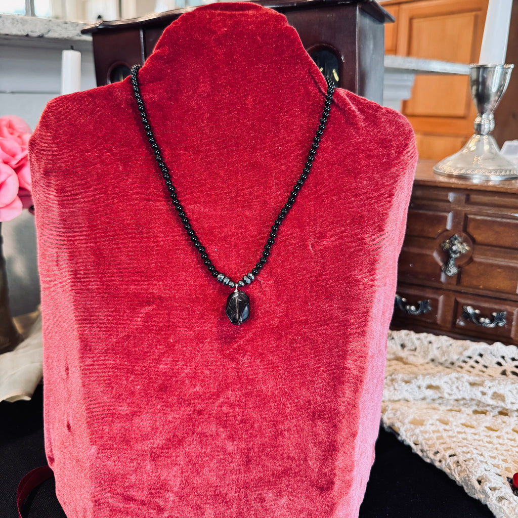 Black beaded Necklace with a Smokey quartz pendant on a red velvet mannequin bust.
