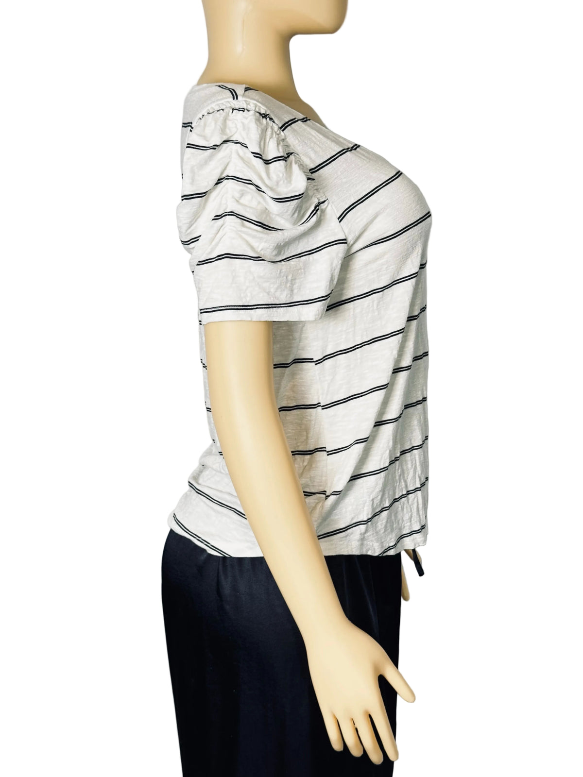 A side-profile view of a short-sleeve top on a mannequin, featuring a white base with thin black horizontal stripes and a gathered, ruffled neckline. The top is styled with dark navy pants against a light gray fabric backdrop.