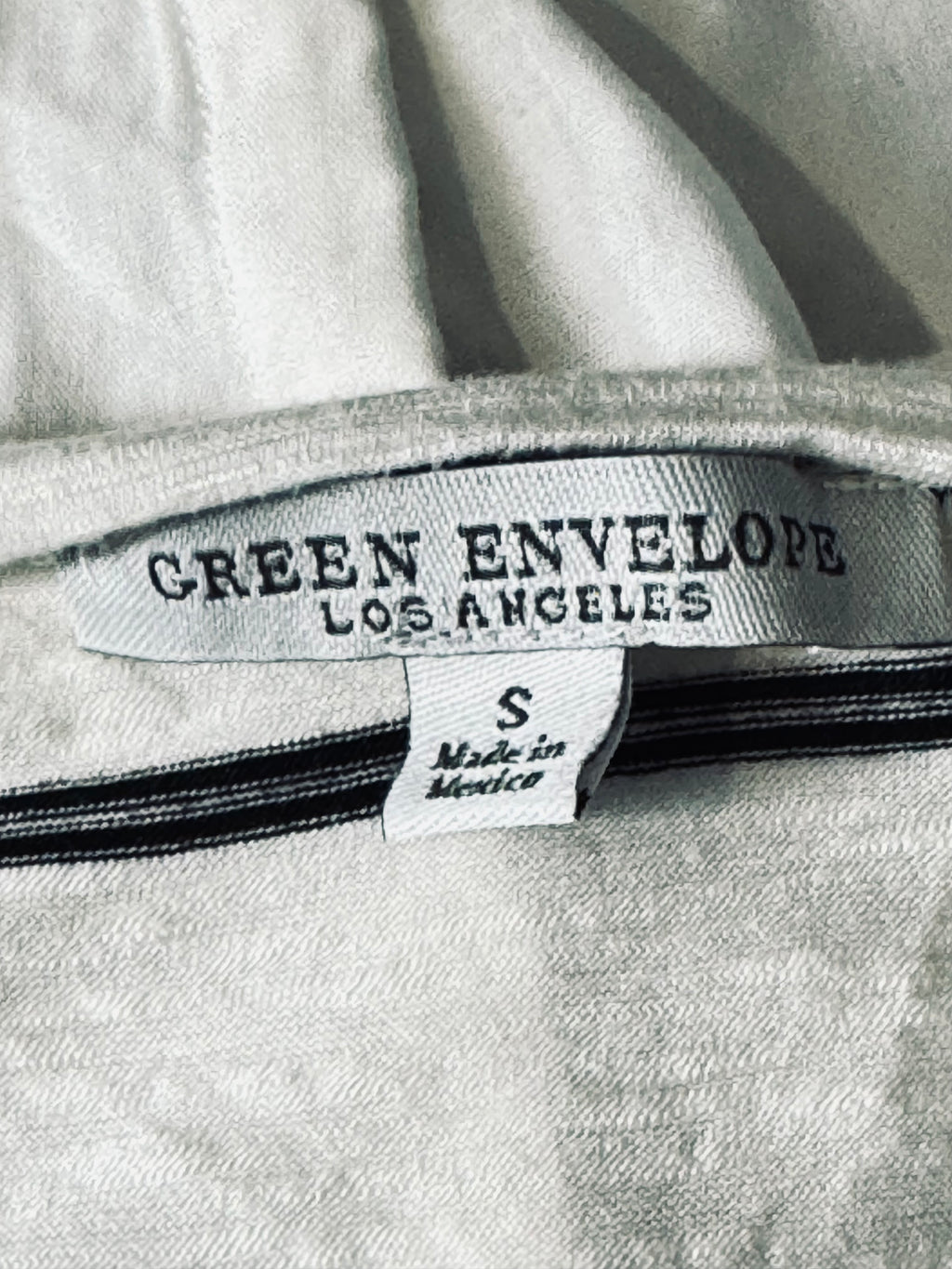Close-up of a light gray fabric garment showing the interior neck label with 'GREEN ENVELOPE LOS ANGELES' and a smaller 'S Made in Mexico' tag.