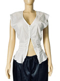 A sleeveless white top with a deep V-neck, gathered side details, and a split front opening, displayed on a beige mannequin torso paired with dark pants against a light gray backdrop.