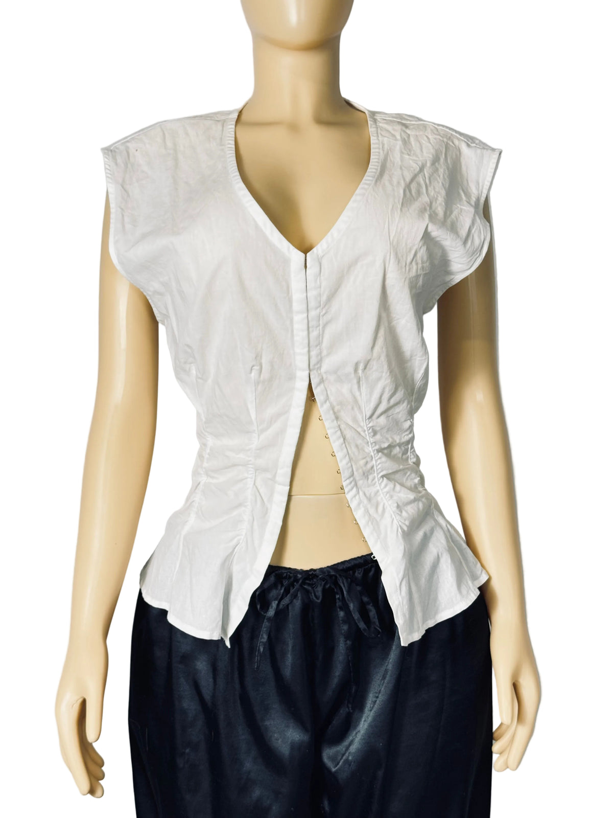 A sleeveless white top with a deep V-neck, gathered side details, and a split front opening, displayed on a beige mannequin torso paired with dark pants against a light gray backdrop.
