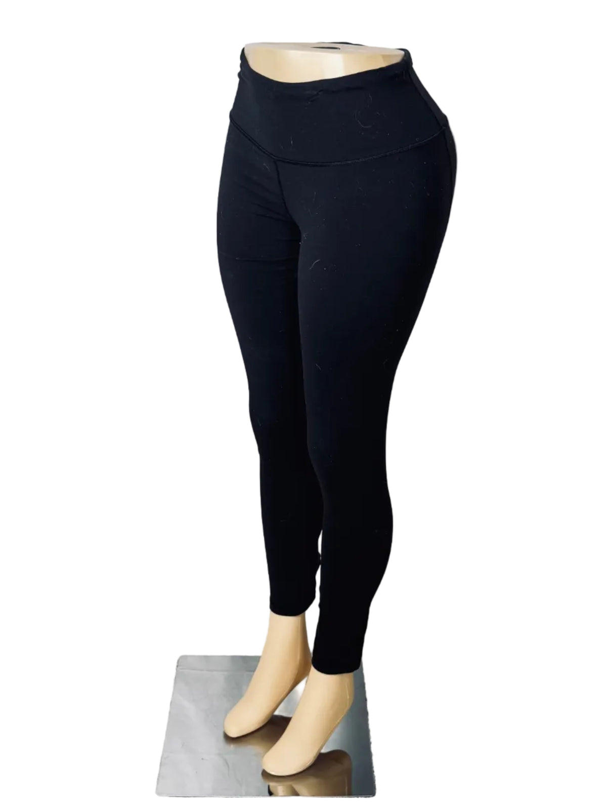 Black high-waisted leggings displayed on a mannequin lower torso with beige feet, set against a white fabric backdrop in a room with carpet and a door.
