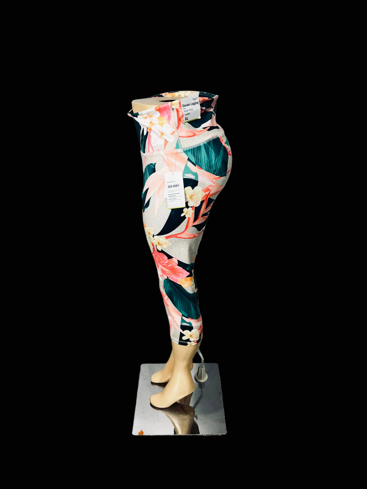 A pair of high-waisted leggings with a vibrant tropical floral print, displayed on a mannequin lower body standing on a mirrored base against a white fabric backdrop.