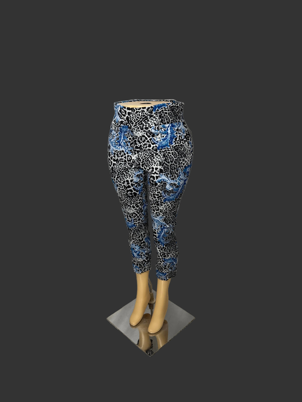Patterned ankle-length capri pants displayed on a mannequin lower body with beige legs, standing on a small metallic base against a white draped backdrop.