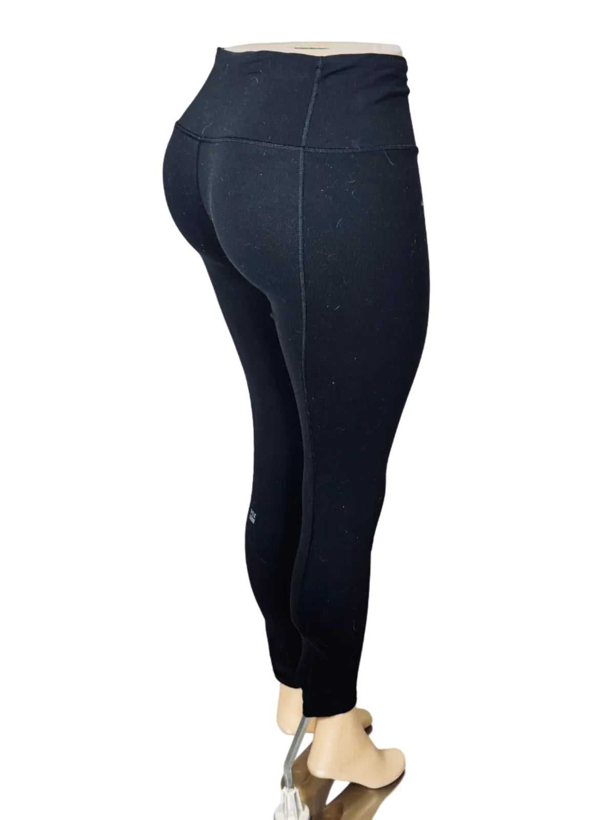 Black high-waisted leggings displayed on a mannequin lower body standing on a small mirror pad in front of a white fabric backdrop.