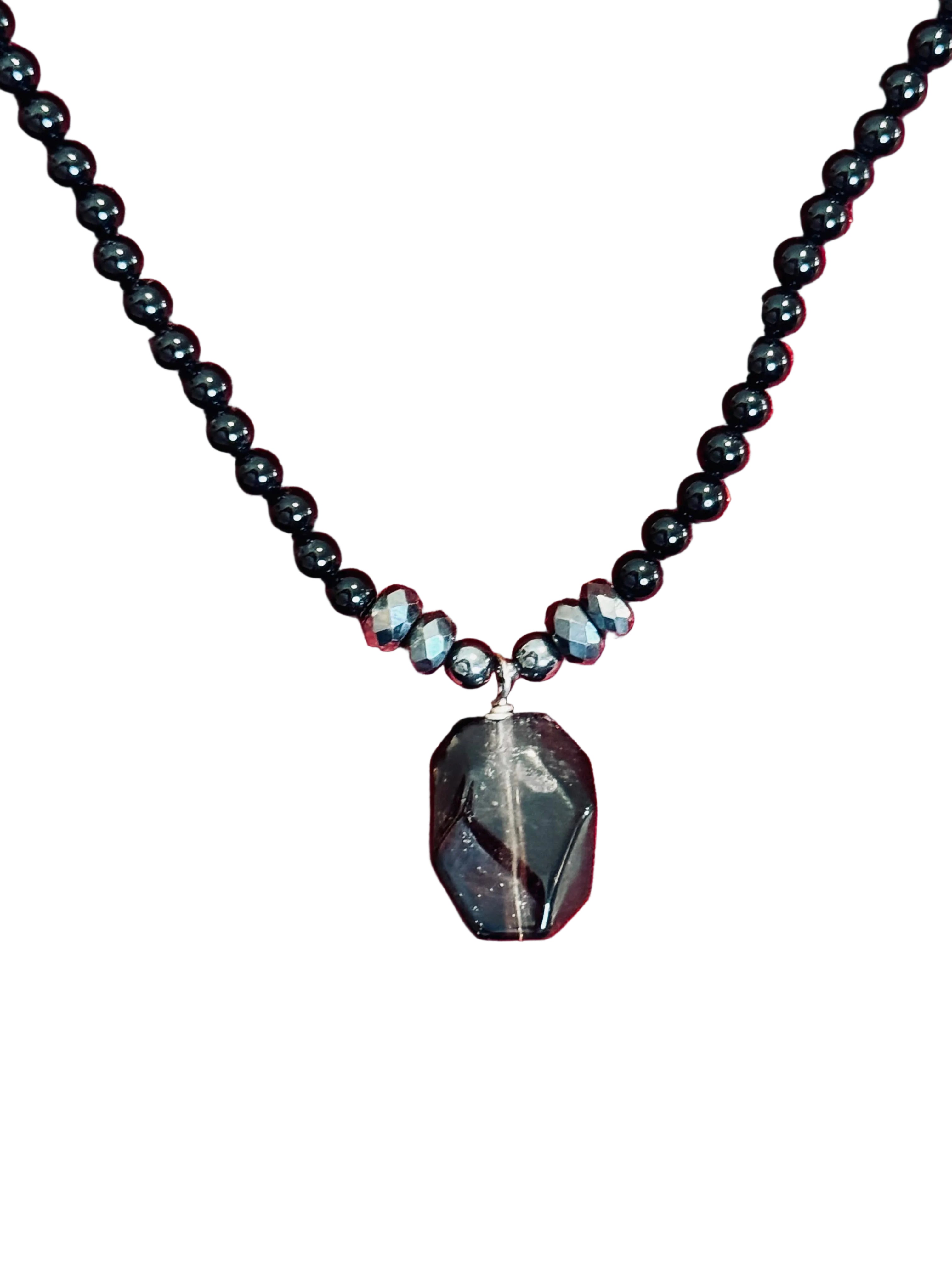 Black beaded Necklace with a Smokey quartz pendant on a red velvet background. 